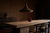 Fumed oak dining room with a single sculptural pendant suspended 32 inches above a travertine table, tadelakt walls in shadow.